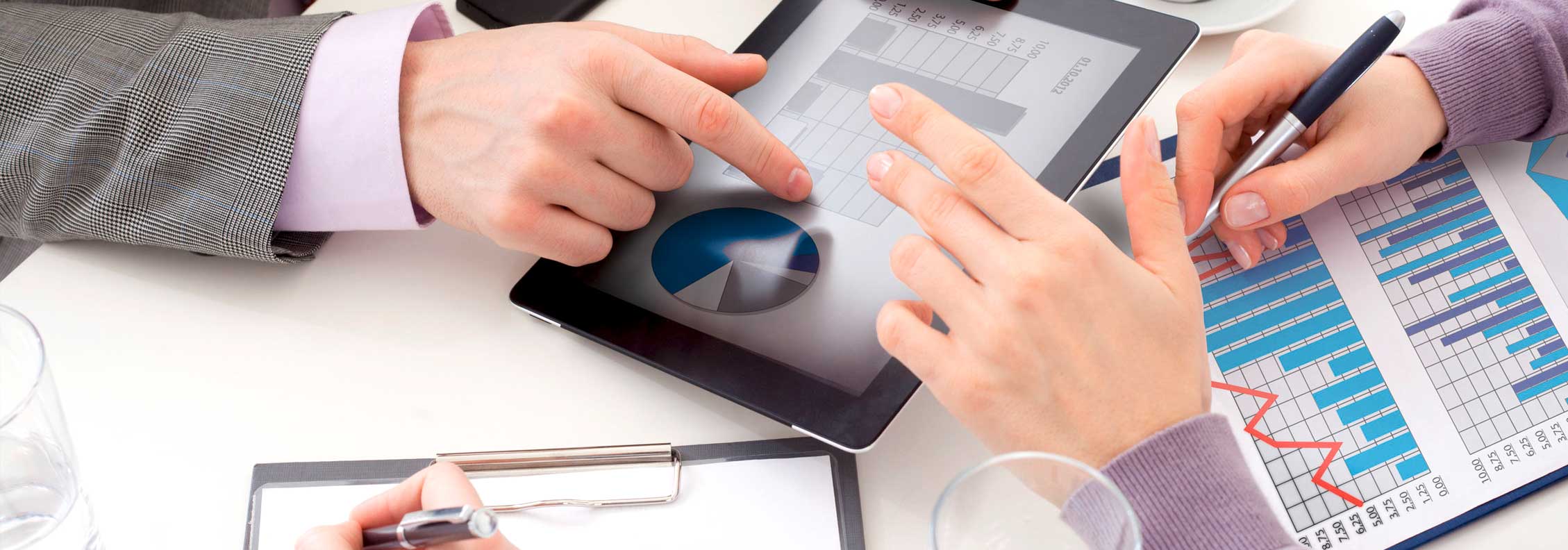 Hände von zwei Personen auf einem Schreibtisch mit Tablet und statistischen Auswertungen, IT Management